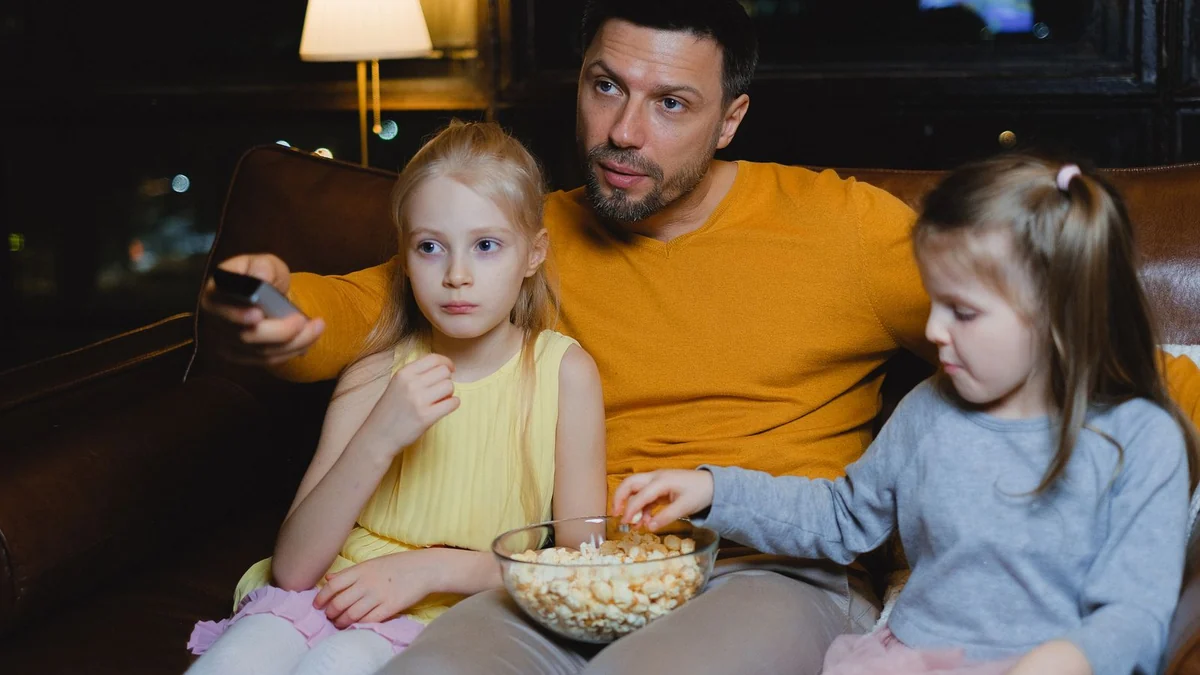A parent and two children watching a film together with popcorn