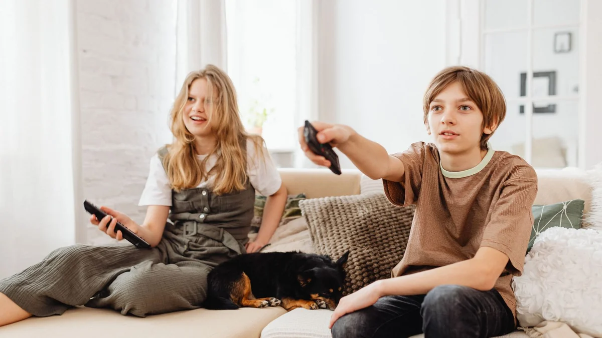 Two children sitting on a sofa with a dog watching television