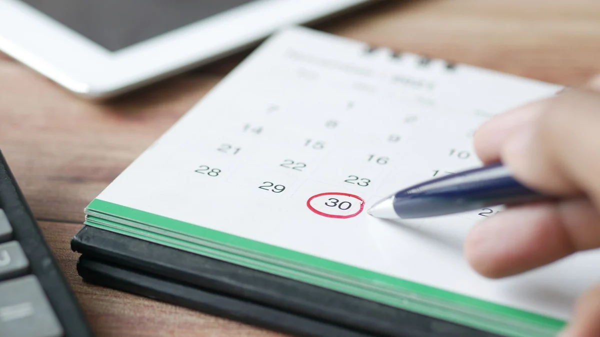 A hand marking a date on a wall calendar with a pen