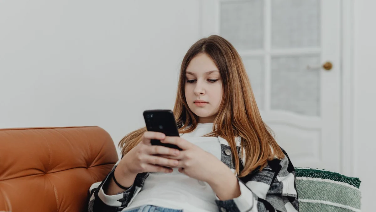 A young person lounging on a sofa scrolling through a phone