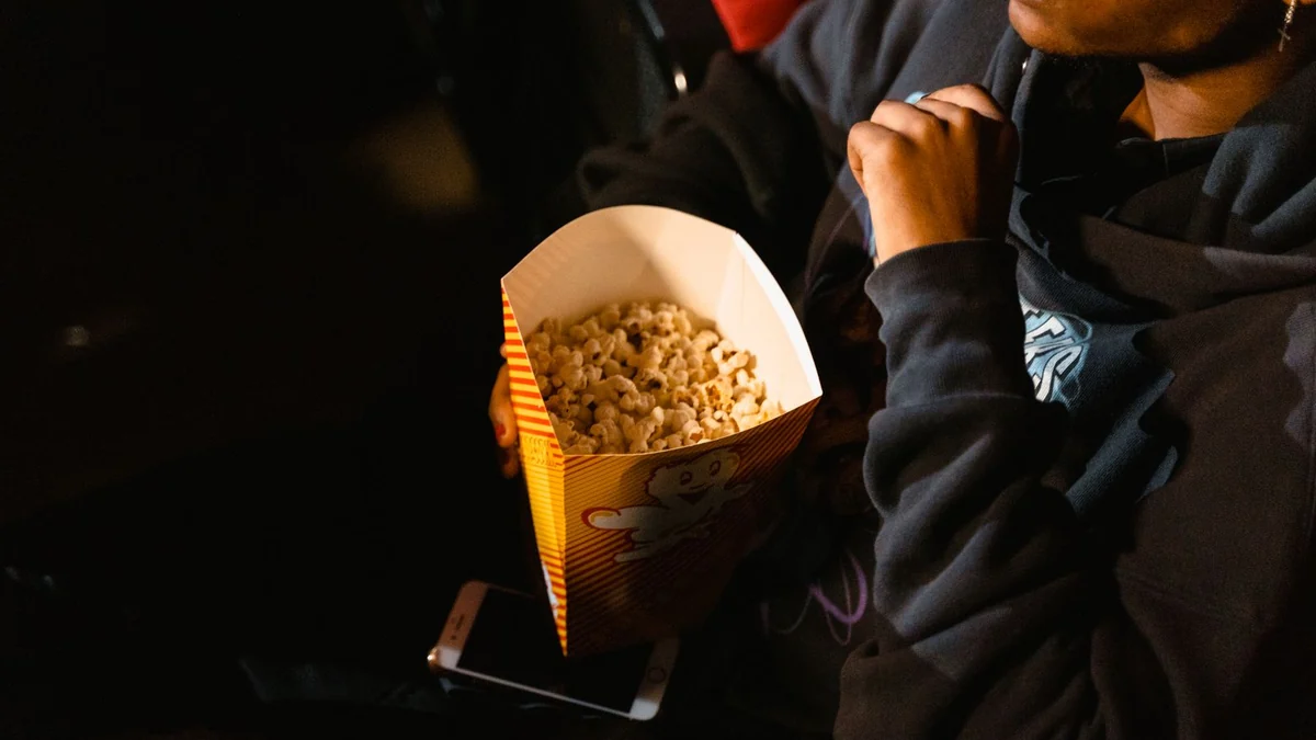 A person holding a box of popcorn in a darkened cinema