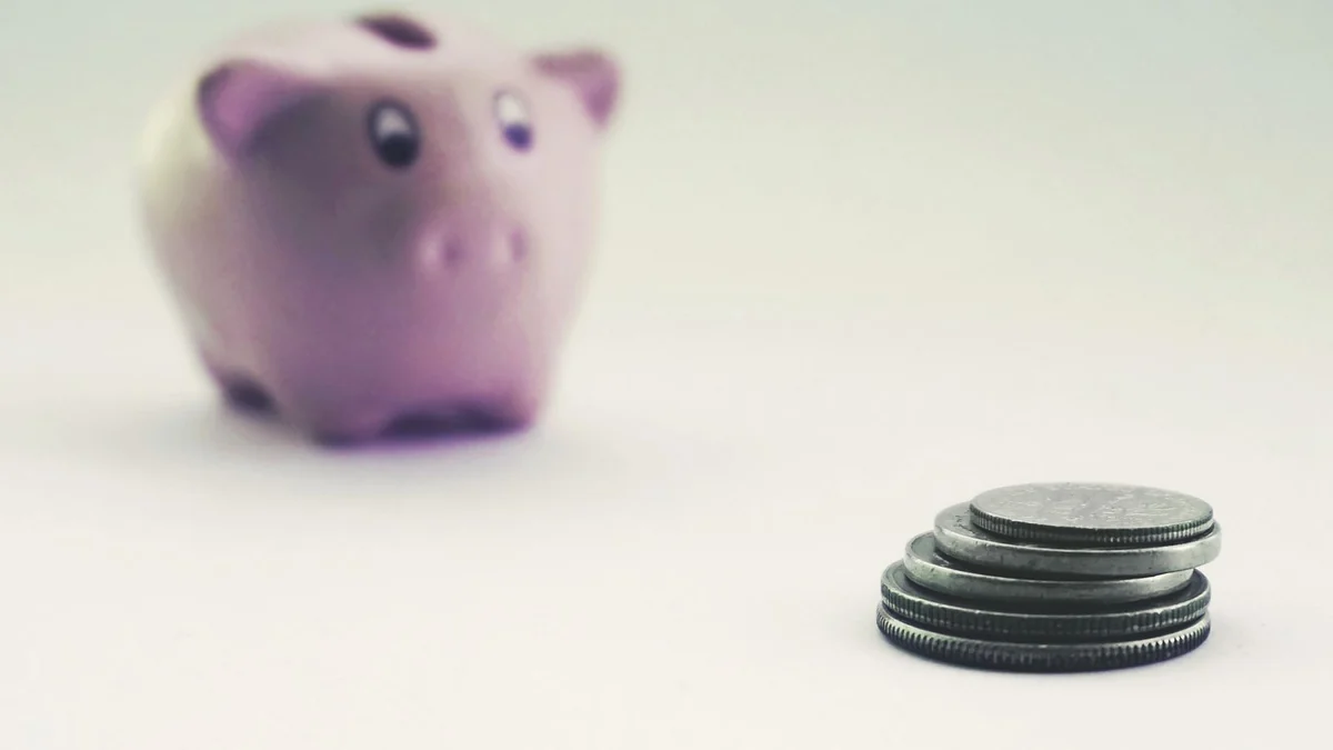 A pink piggy bank beside stacked coins