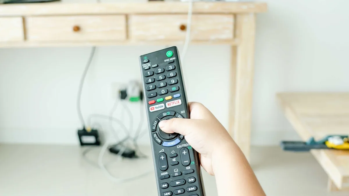 A hand holding a television remote control with a streaming shortcut button