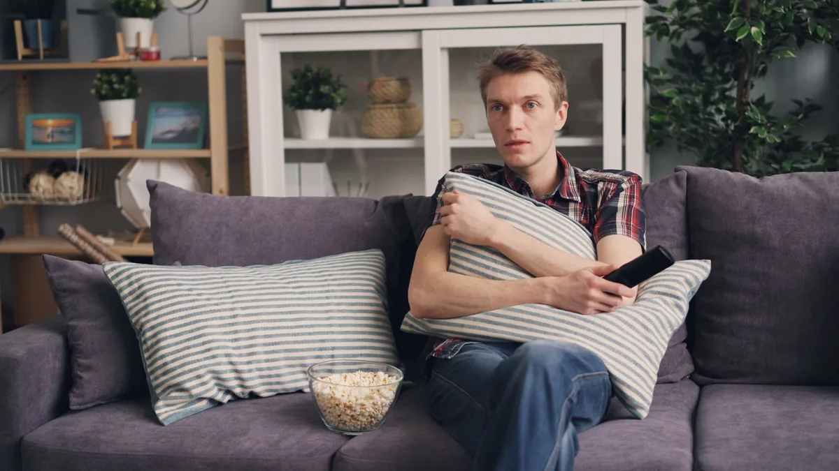 A man watching television on a sofa with a bowl of popcorn