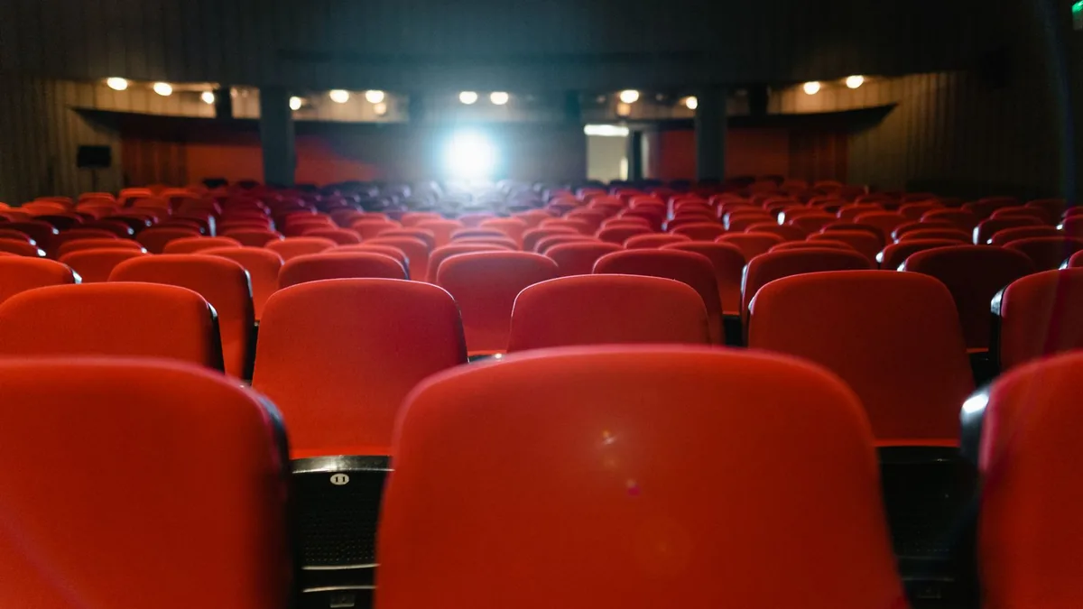 Rows of empty red cinema seats facing a lit screen